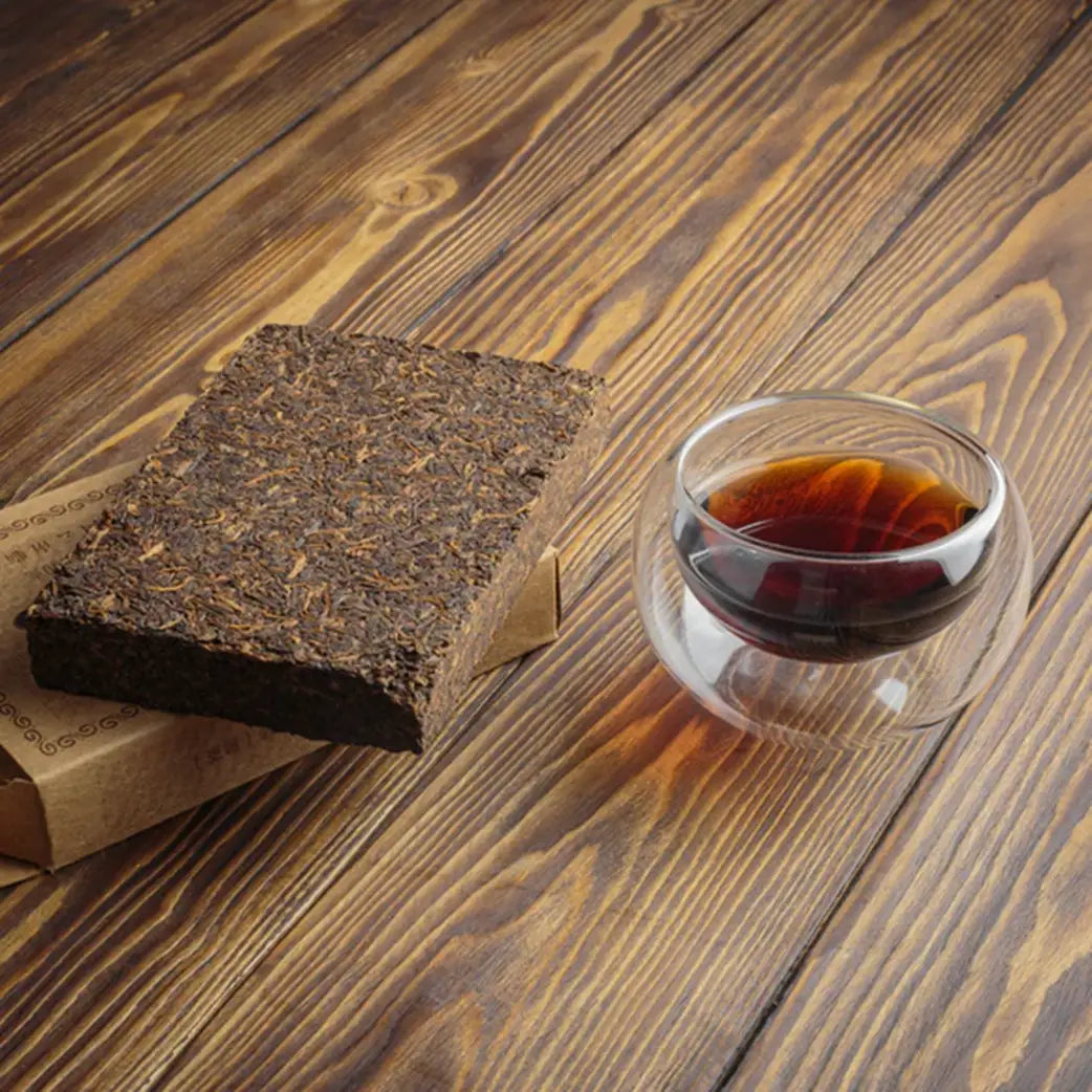 Compressed Pu Erh tea brick with a glass of brewed Pu Erh tea on a wooden surface