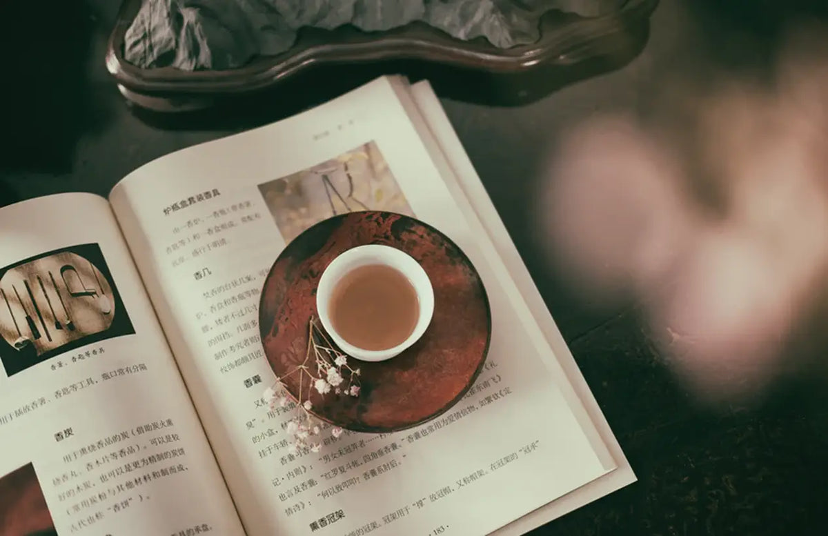 Open book and teacup on a wooden table representing Chinese Tea culture